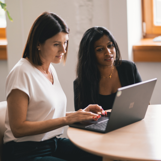 Imagen de dos mujeres sentadas ante un escritorio y mirando un ordenador.